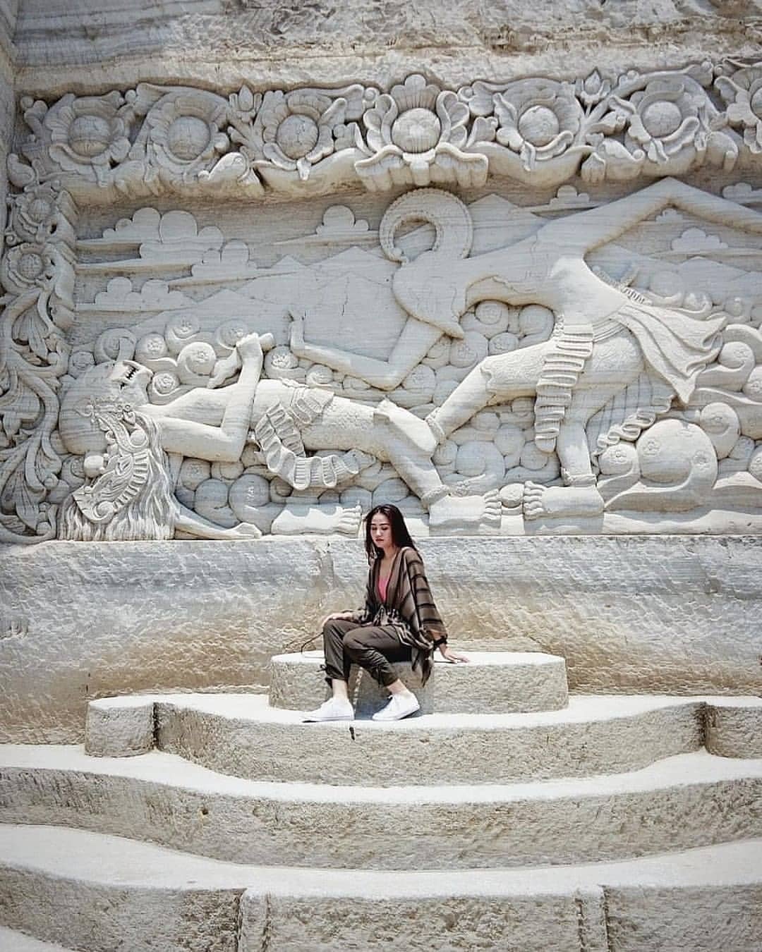 Woman sitting on steps in front of artistic carvings on Breksi Cliff.