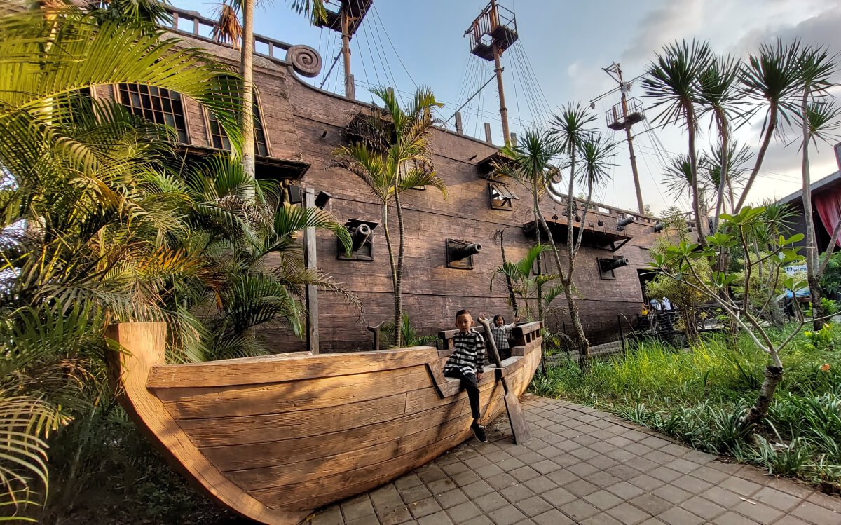 Children sitting on a wooden ship structure next to a large pirate ship at Waterboom Jogja.