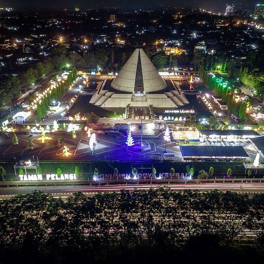 An aerial view of Taman Pelangi in Yogyakarta at night, showing colorful lights and the Monumen Jogja Kembali.