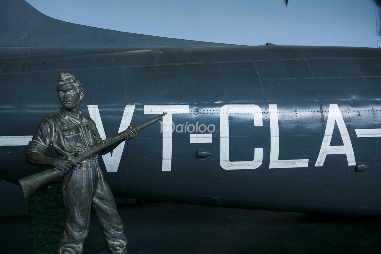 A statue of a soldier holding a rifle in front of a large military aircraft with the letters "VT-CLA" on it.