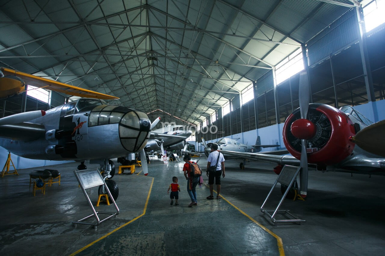 Visitors walking among the various aircraft displayed in a large hangar at the Dirgantara Mandala Museum.