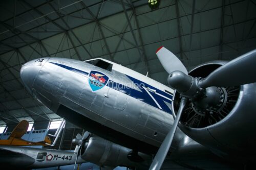 A silver C-47 Dakota airplane on display in a large hangar.