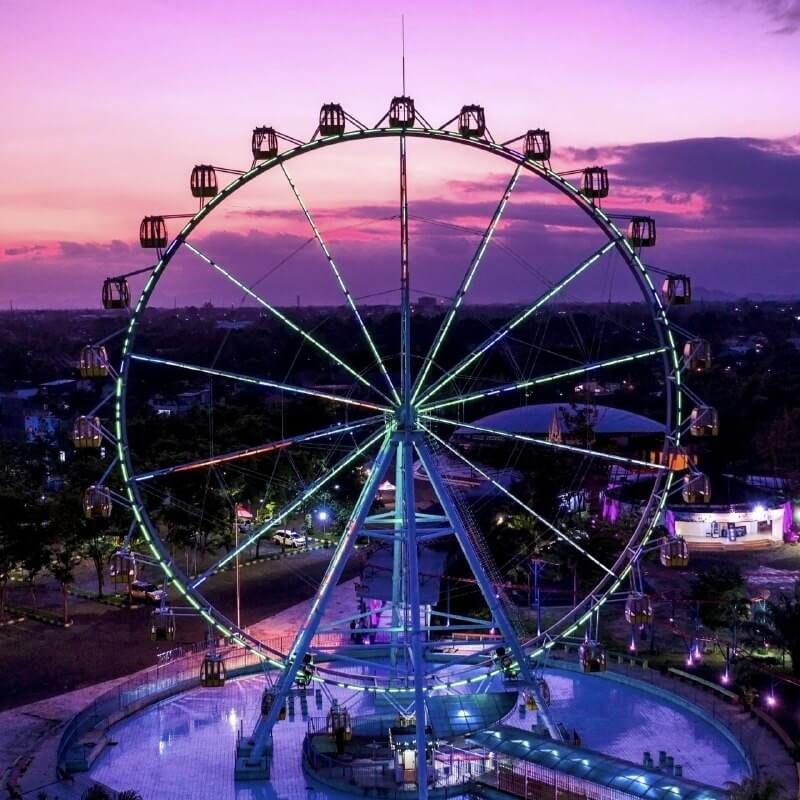 Illuminated Ferris wheel at Sindu Kusuma Edupark during the evening with a purple sky.