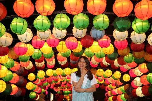 A woman stands smiling under colorful lanterns at Taman Pelangi in Yogyakarta.