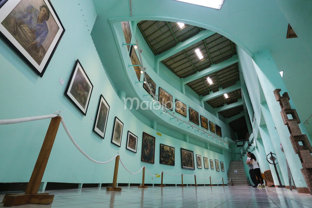 Two people looking at paintings displayed in Affandi Museum's second gallery.