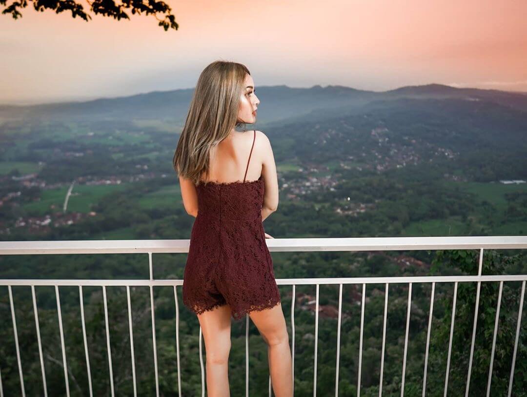 A woman standing at a vantage point at De Mangol View, overlooking a scenic landscape at sunset.