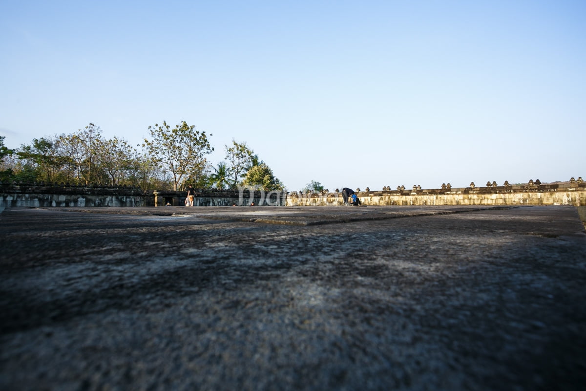 People sit and stand on the flat stone surface of the Pendopo at Ratu Boko Palace.