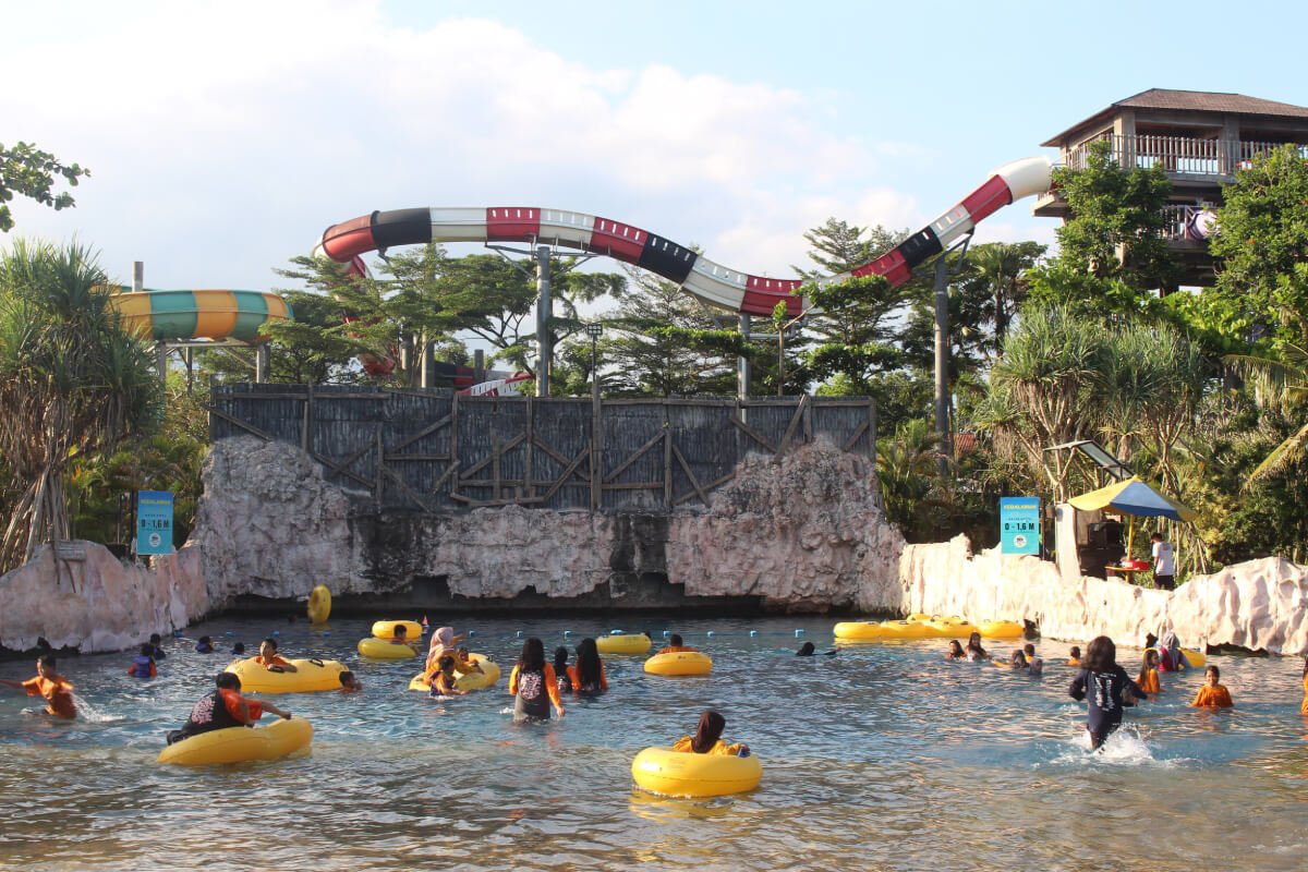 Visitors enjoying the wave pool with water slides in the background at Waterboom Jogja.