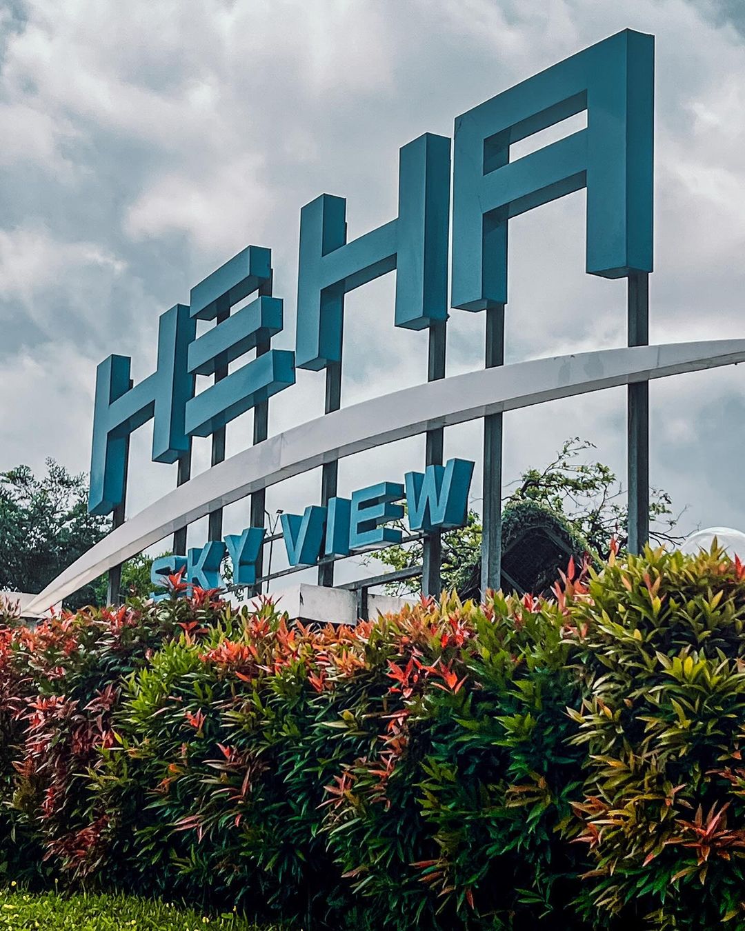 Large blue sign of HeHa Sky View with colorful bushes in front.