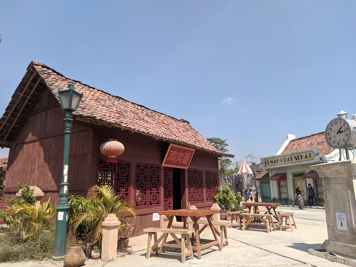 Old-fashioned buildings with a clock and outdoor seating at Gamplong Studio Alam.