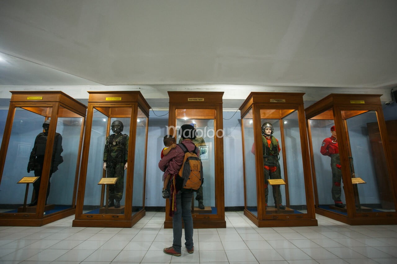 A visitor studying different uniforms used by various divisions of the Indonesian Air Force, displayed in glass cases.