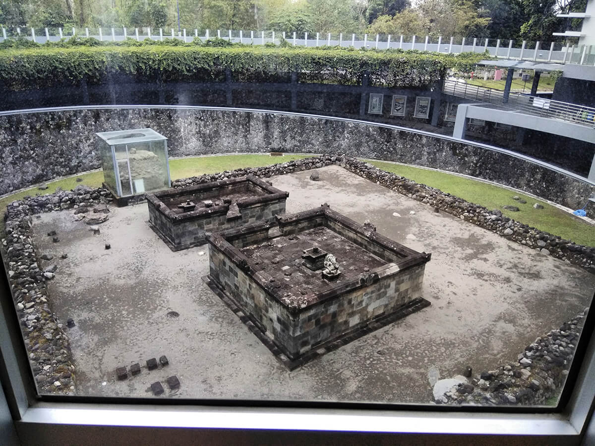 An aerial view of the Kimpulan Temple ruins, located at UII campus in Yogyakarta, featuring stone structures and a glass-protected artifact.