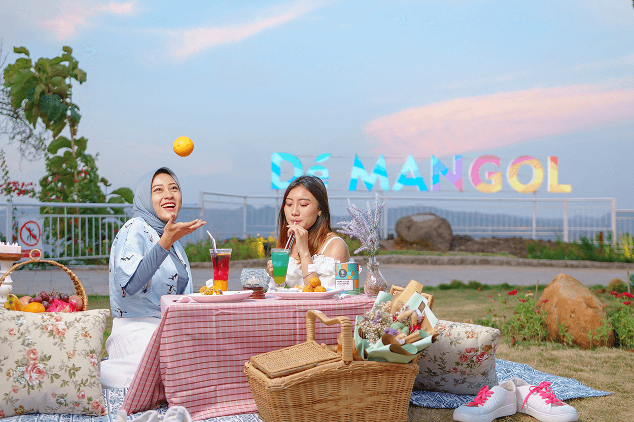 Two women enjoying a picnic at De Mangol View with colorful letters in the background.