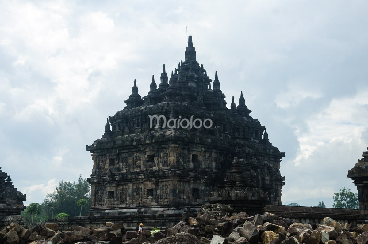 The main temple of Plaosan with stone ruins in the foreground and a cloudy sky.