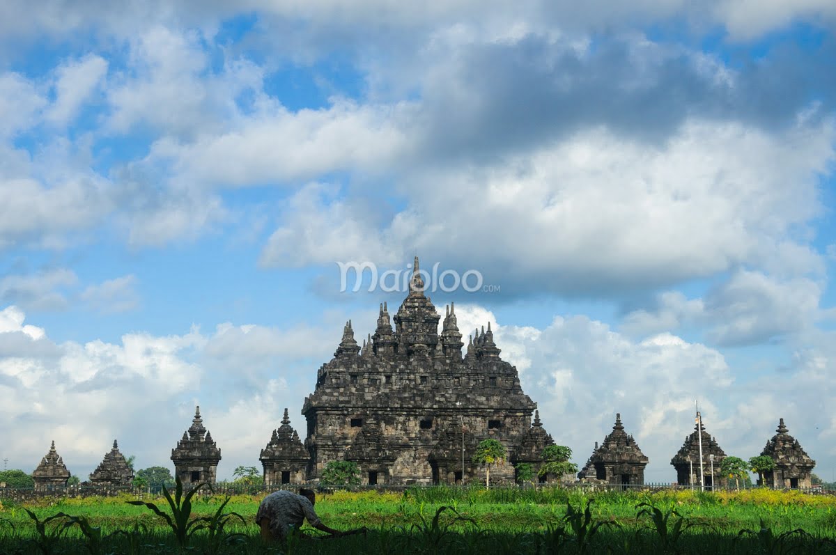 A view of Plaosan Temple with cloudy sky and a person working in the field in the foreground.
