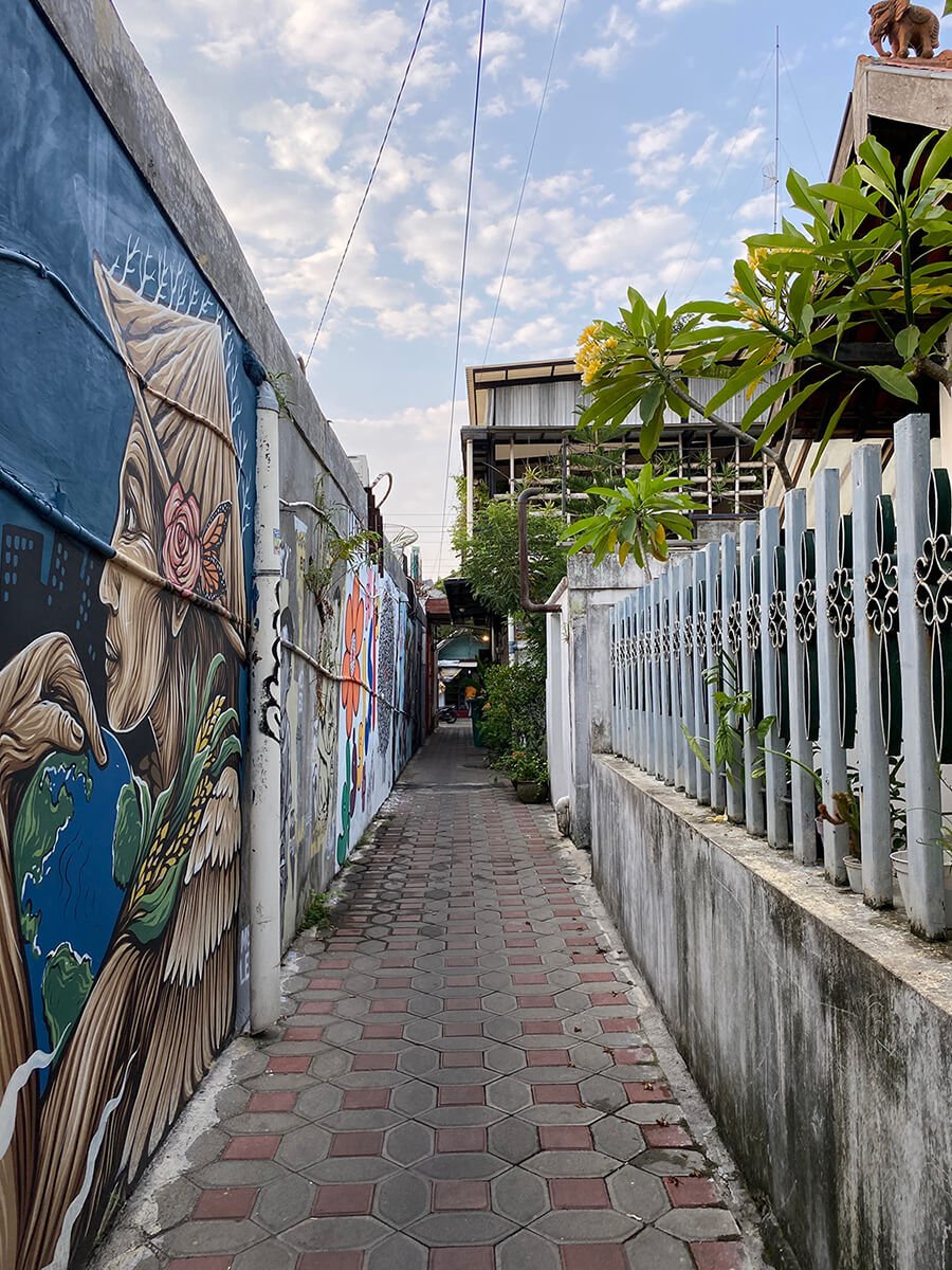 A narrow alley in Prawirotaman with colorful murals on the walls and plants along the sides.