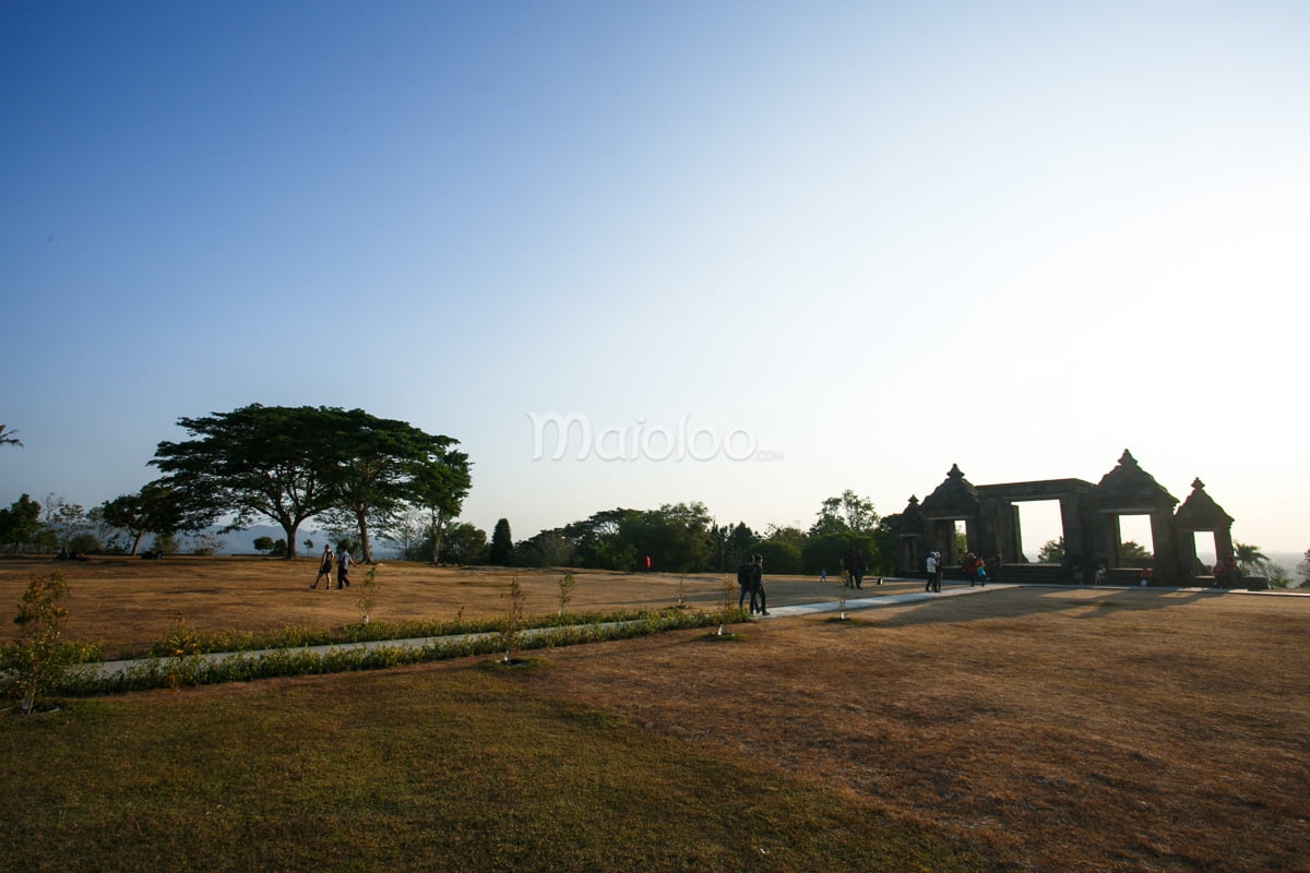 Visitors walking around the expansive grounds of Ratu Boko Palace with the ancient gate in the background.