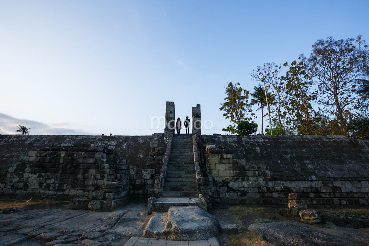 Two people stand at the top of an ancient stone staircase at Ratu Boko Palace.