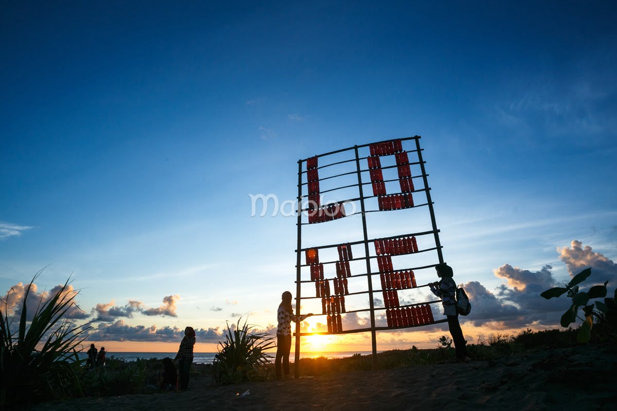 People standing near a recycled bottle installation that spells "LOVE" at sunset.