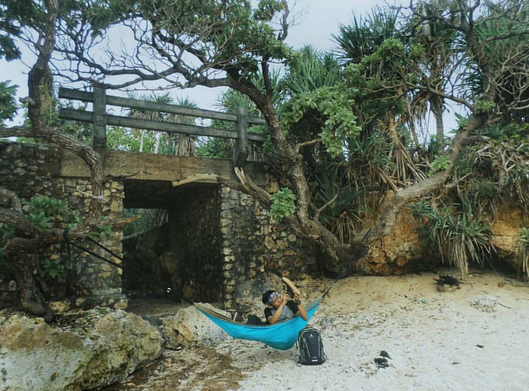 person relaxing in a hammock tied to a tree near a stone bridge at Lolang Beach.