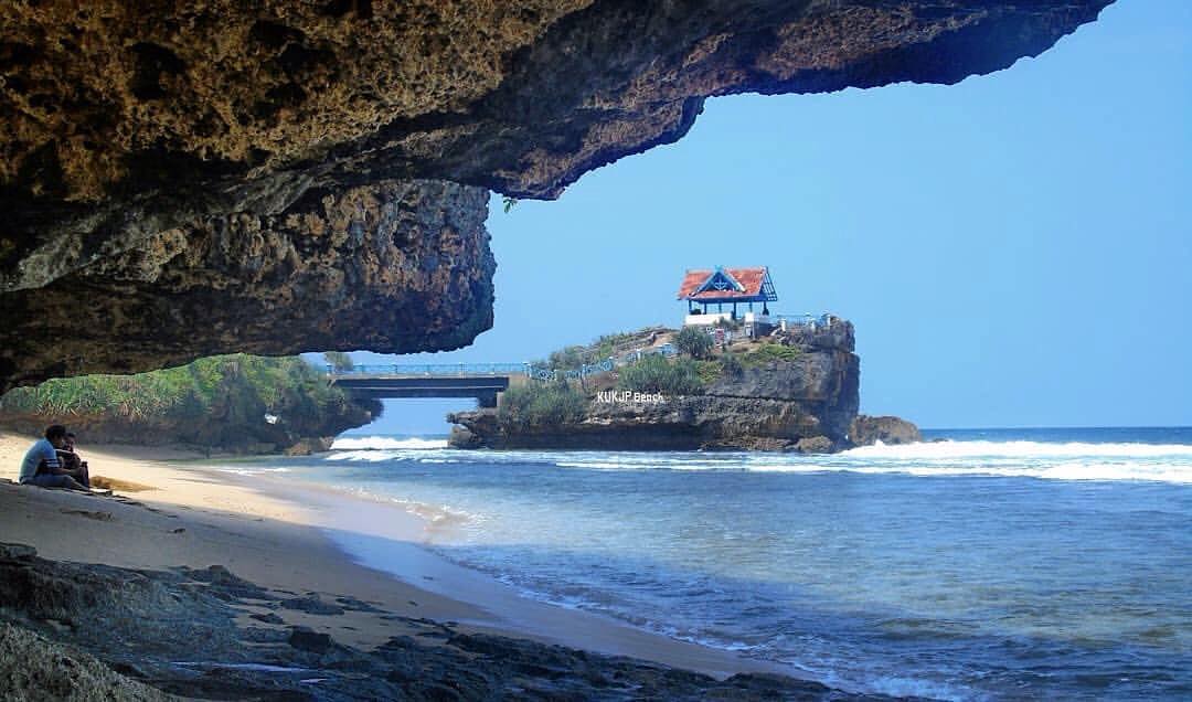 A rocky bridge connecting the mainland to a small island with a pavilion at Kukup Beach.