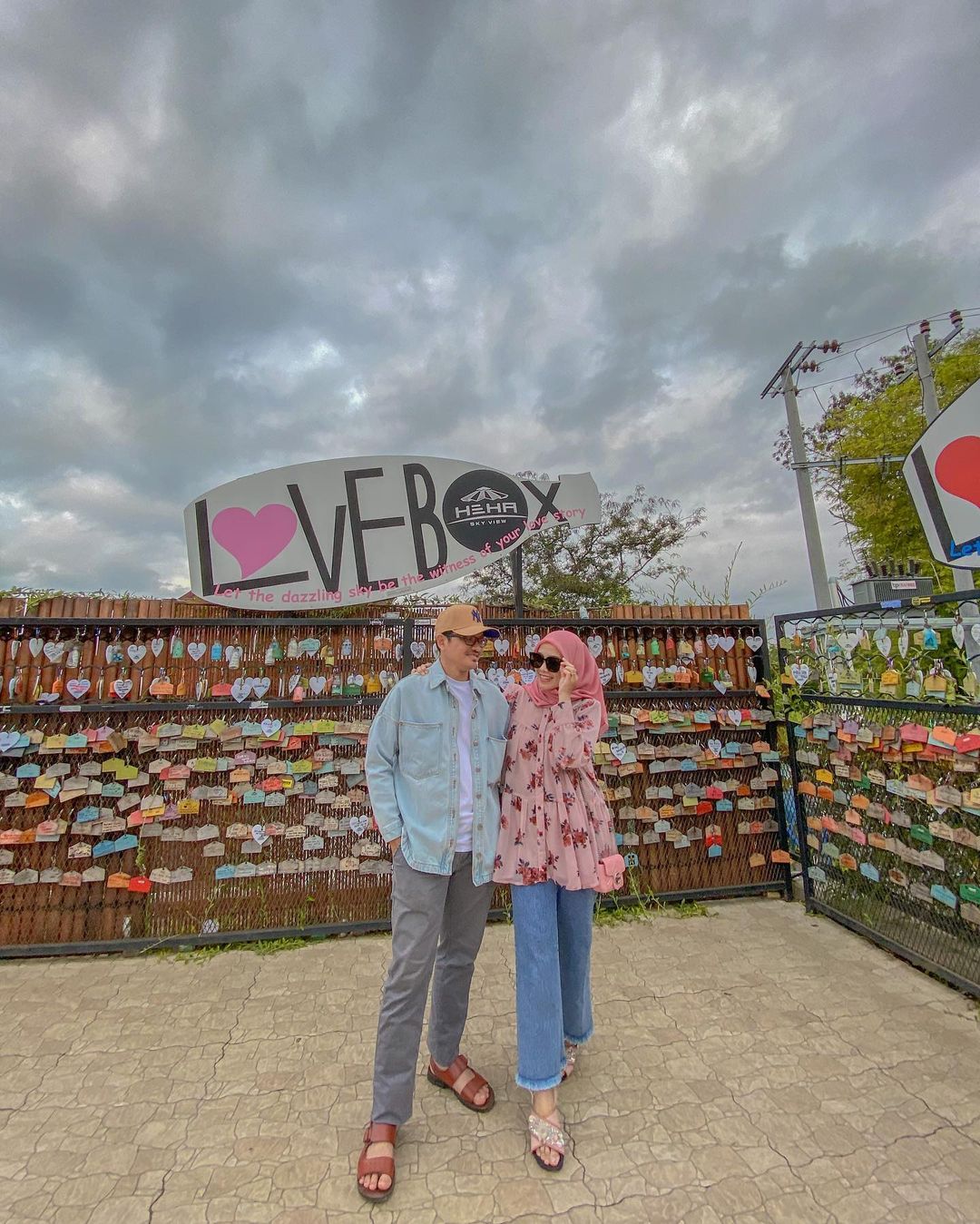 A couple standing in front of the Love Box area at HeHa Sky View, surrounded by locks with messages.