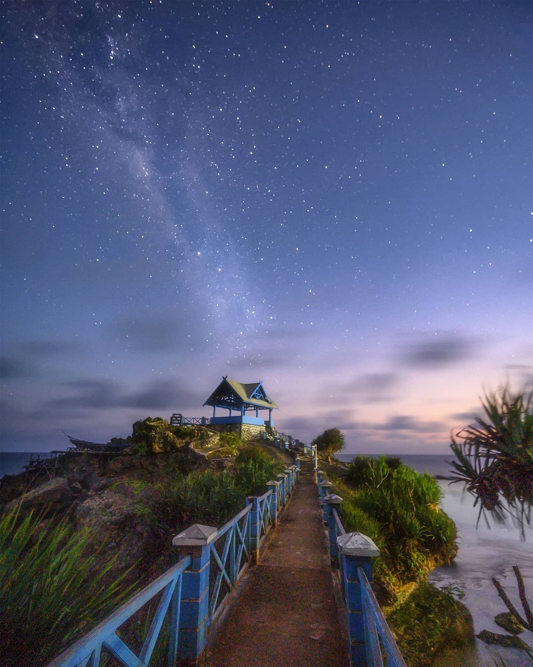 A starry sky over the pavilion on the rocky island connected by a bridge at Kukup Beach.