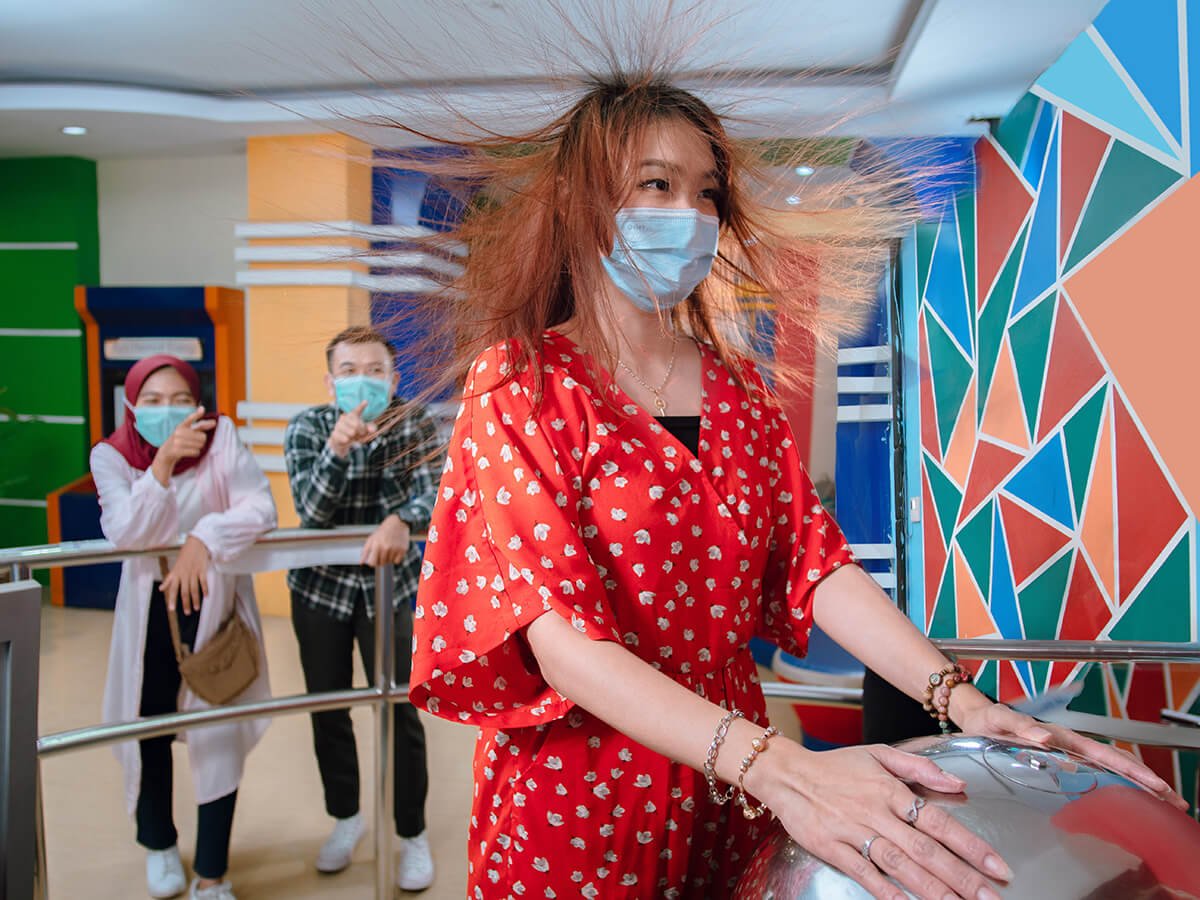 A visitor experiencing static electricity with her hair standing up at the Van De Graaf generator in Taman Pintar.