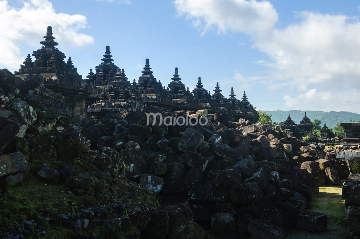 View of numerous stupas and stone ruins at Plaosan Temple complex under a blue sky.