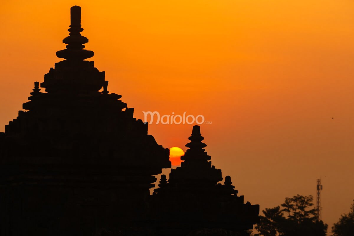 Silhouette of Plaosan Temple's spires against a vibrant orange sunset.