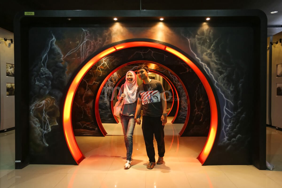 Two visitors walking through an illuminated simulation tunnel at the Merapi Volcano Museum.