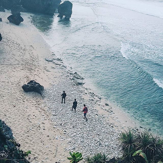 Three people walking on the sandy shore of Pringjono Beach.