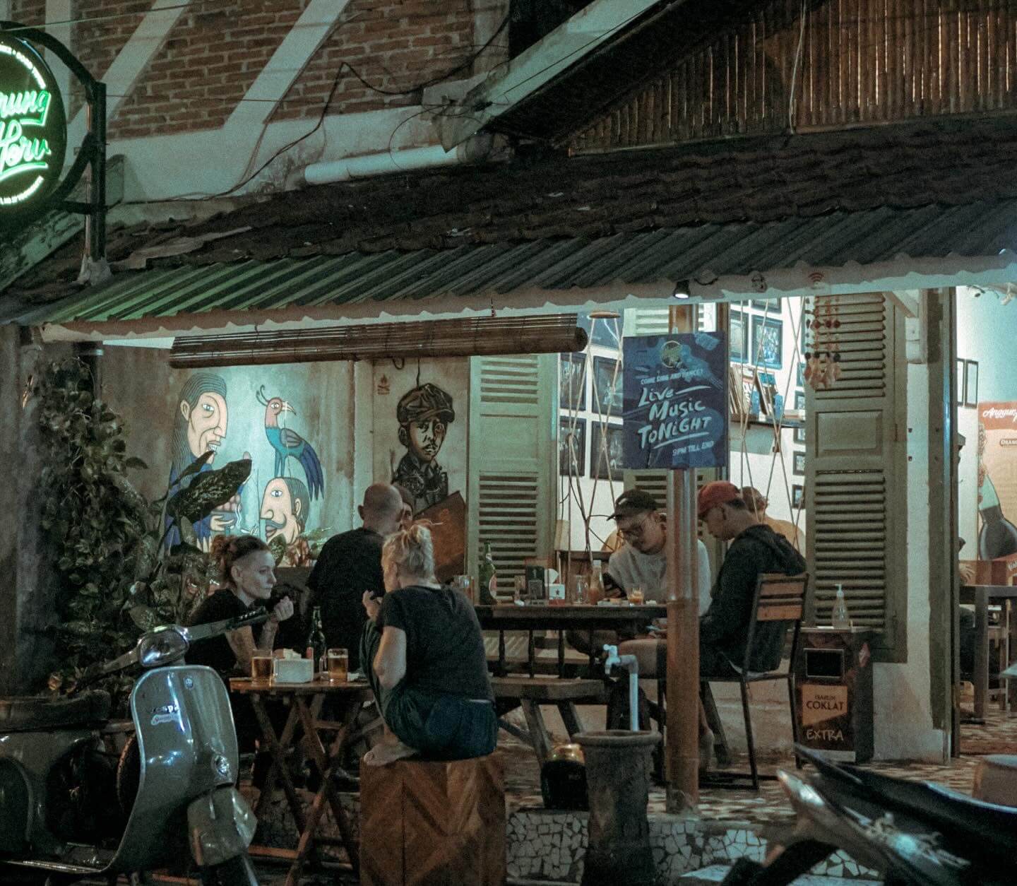 People sitting and enjoying food outside Warung Heru in Prawirotaman, with colorful murals in the background.