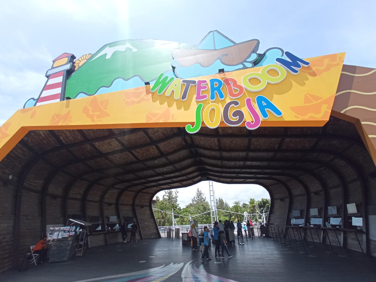 Entrance of Waterboom Jogja with a colorful sign and visitors walking underneath.