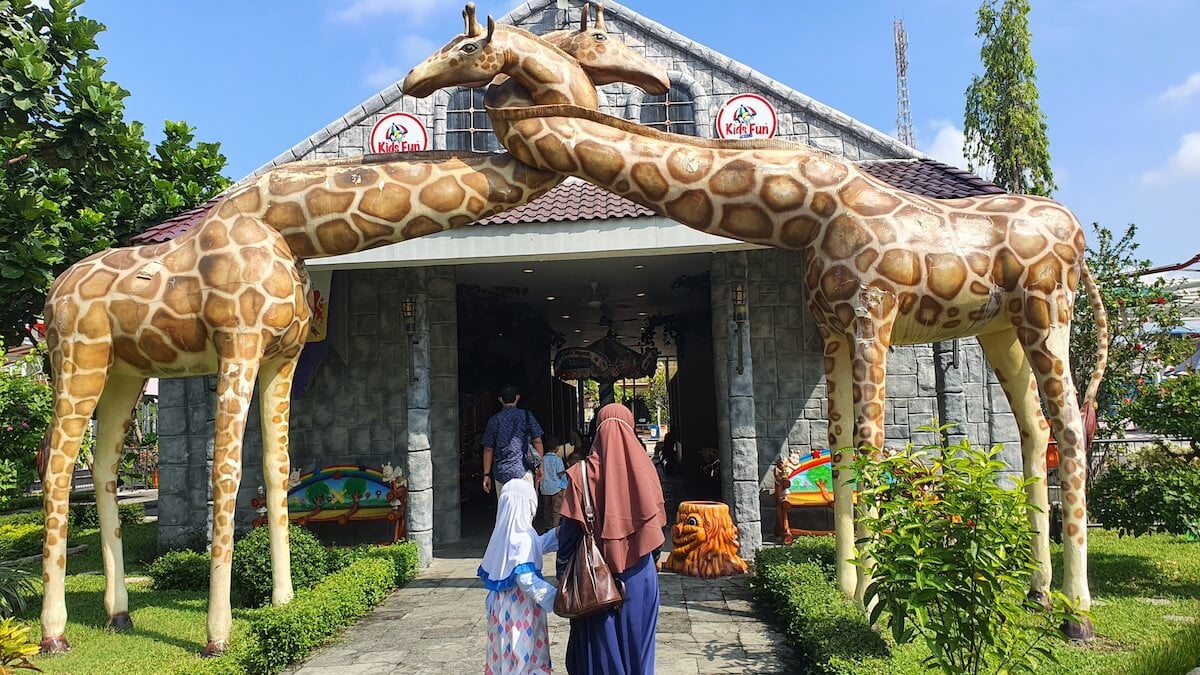 Entrance of Kids Fun Park with large giraffe statues arching over visitors walking in.