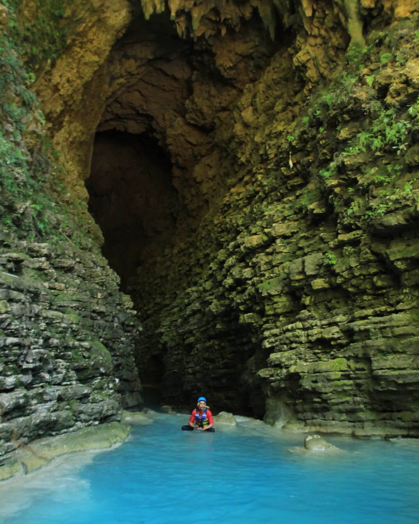 A person in a safety helmet and vest enjoying the blue waters within a cave at Kalisuci Cave Tubing.