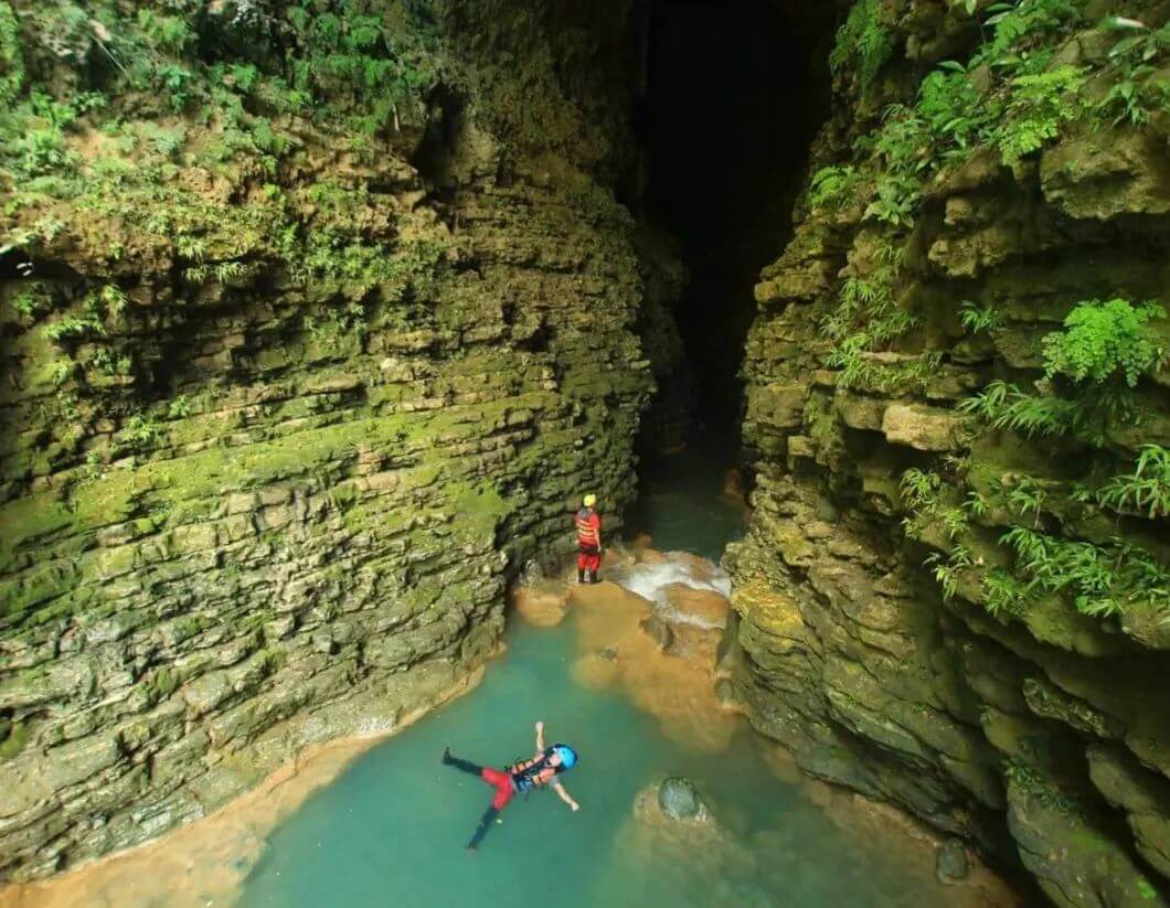 Two people enjoying cave tubing in the clear waters of Kalisuci, surrounded by lush green walls.