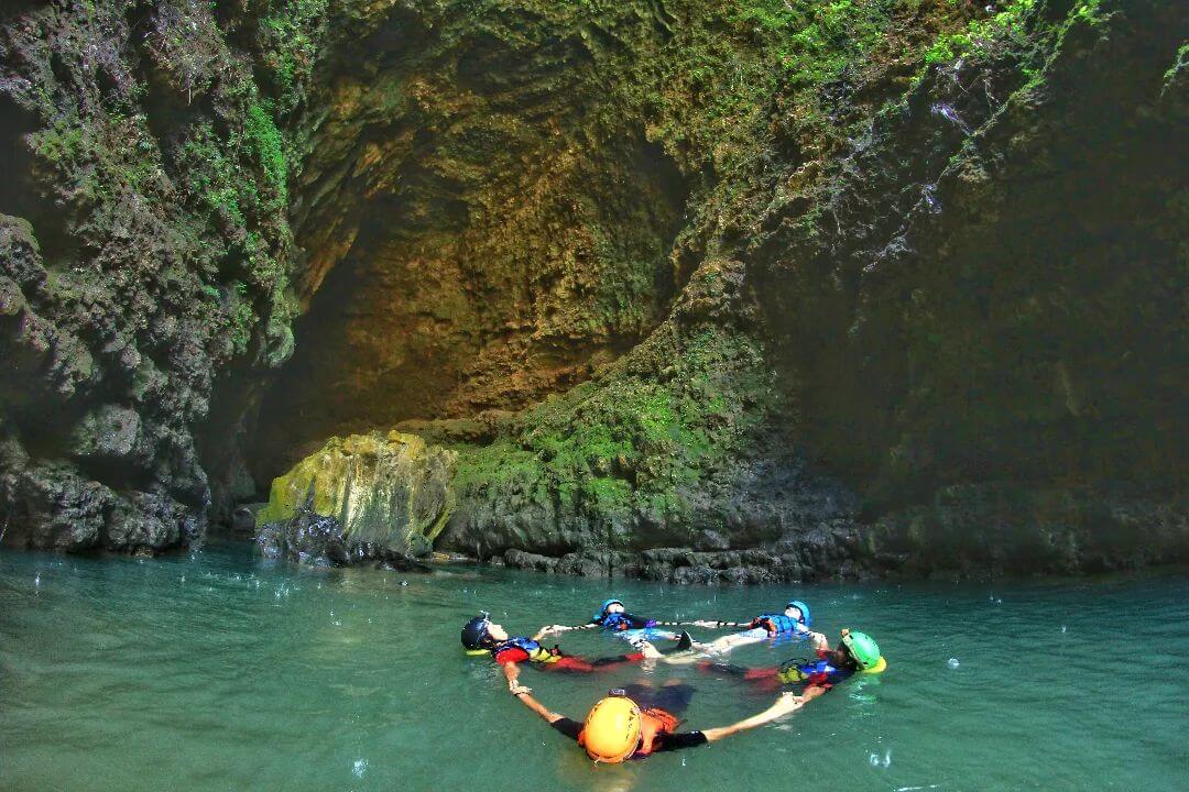 A group of people forming a circle while floating in the clear water inside a cave at Kalisuci.