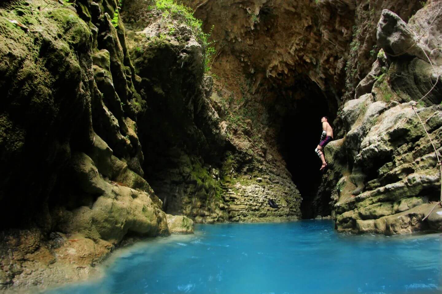 A person mid-jump into the bright blue waters at the entrance of a cave in Kalisuci.