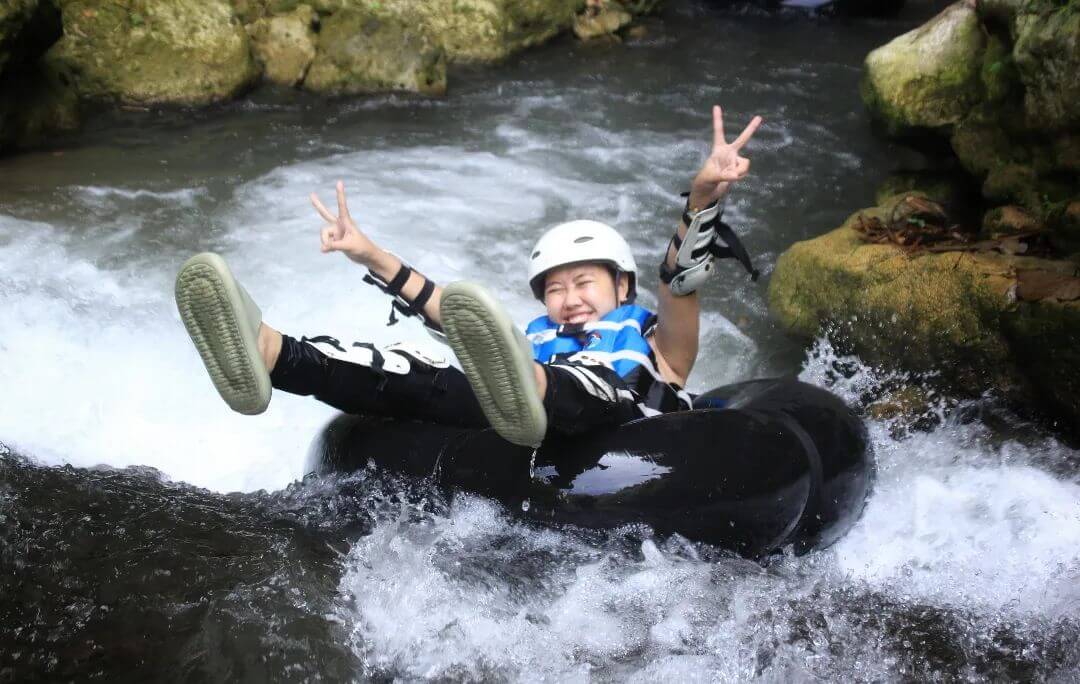 A person smiling and posing with peace signs while sitting in a rubber tube on a river in Kalisuci.