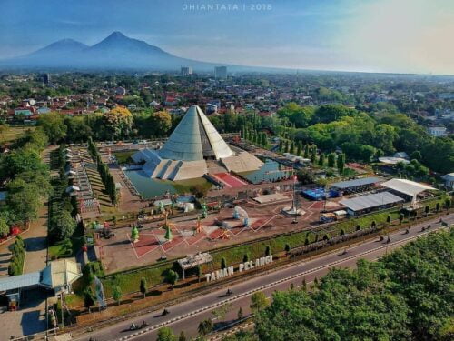 Aerial view of Monumen Jogja Kembali with its distinctive cone-shaped structure, surrounded by lush greenery and cityscape in Yogyakarta.