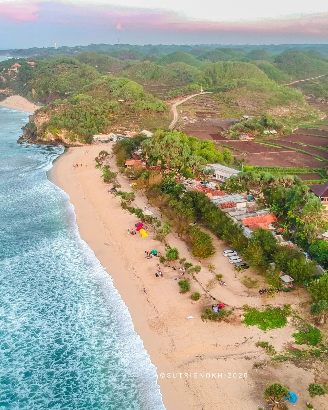 Aerial view of Watu Kodok Beach with blue ocean waves, sandy shore, and green hills.