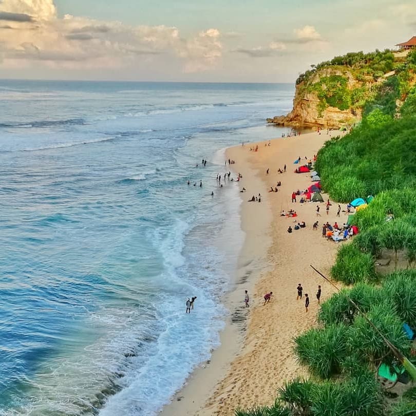 People enjoying activities on the sandy shore of Sanglen Beach with colorful tents and lush greenery nearby.