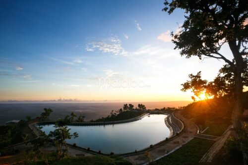 A large, heart-shaped water reservoir on top of a mountain during sunset.