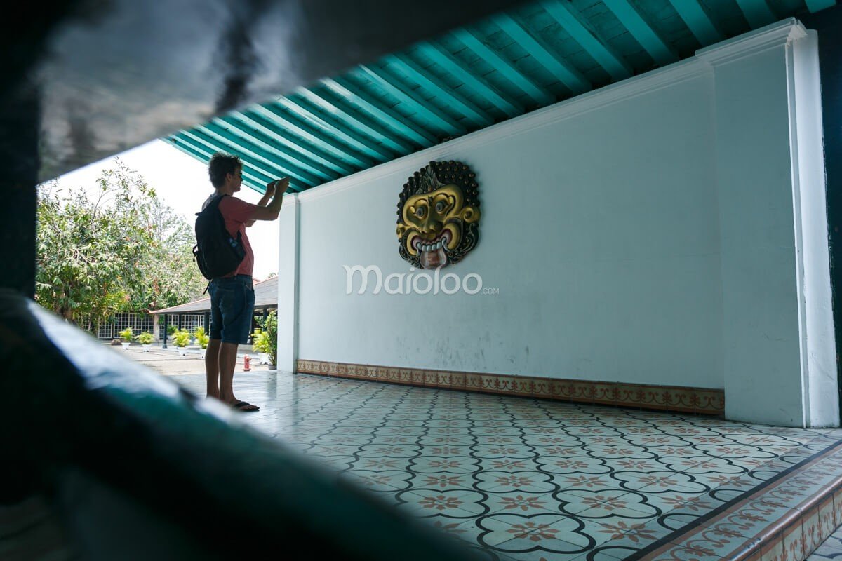 A tourist taking a photo of a traditional mask on a wall in the Sri Manganti Complex at Yogyakarta Palace.