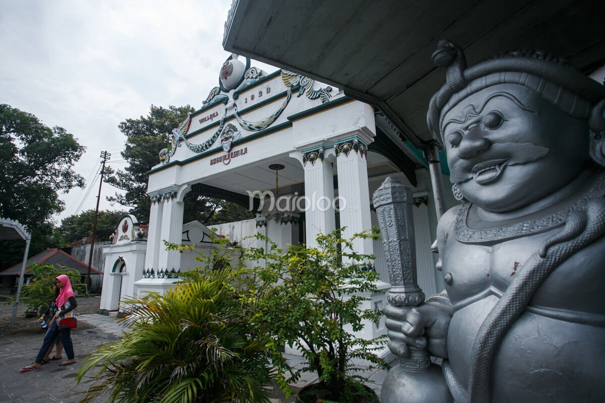 The Donopratopo Gate at Yogyakarta Palace with a statue and people walking nearby.