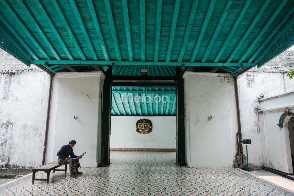 Entrance to the Sri Manganti Complex at Yogyakarta Palace, with a person sitting on a bench reading a paper.