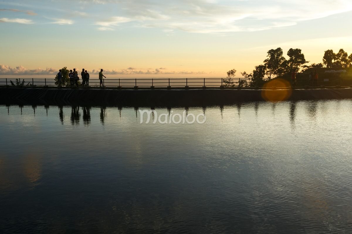 People standing by the edge of a reservoir with a sunset backdrop.