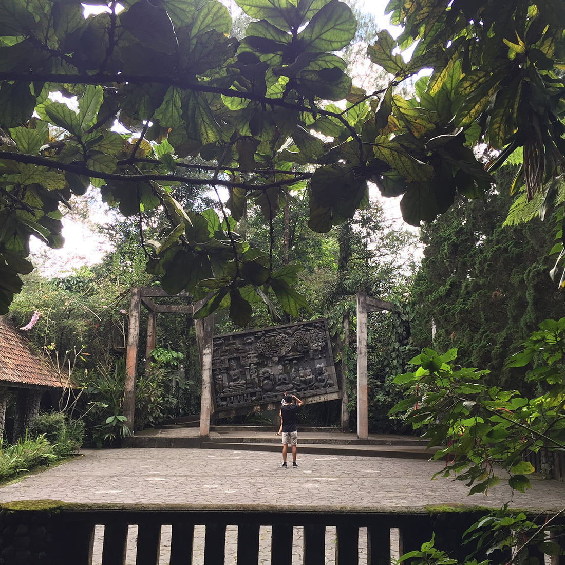 A person stands at a courtyard with large stone carvings surrounded by thick greenery at Ullen Sentalu Museum.