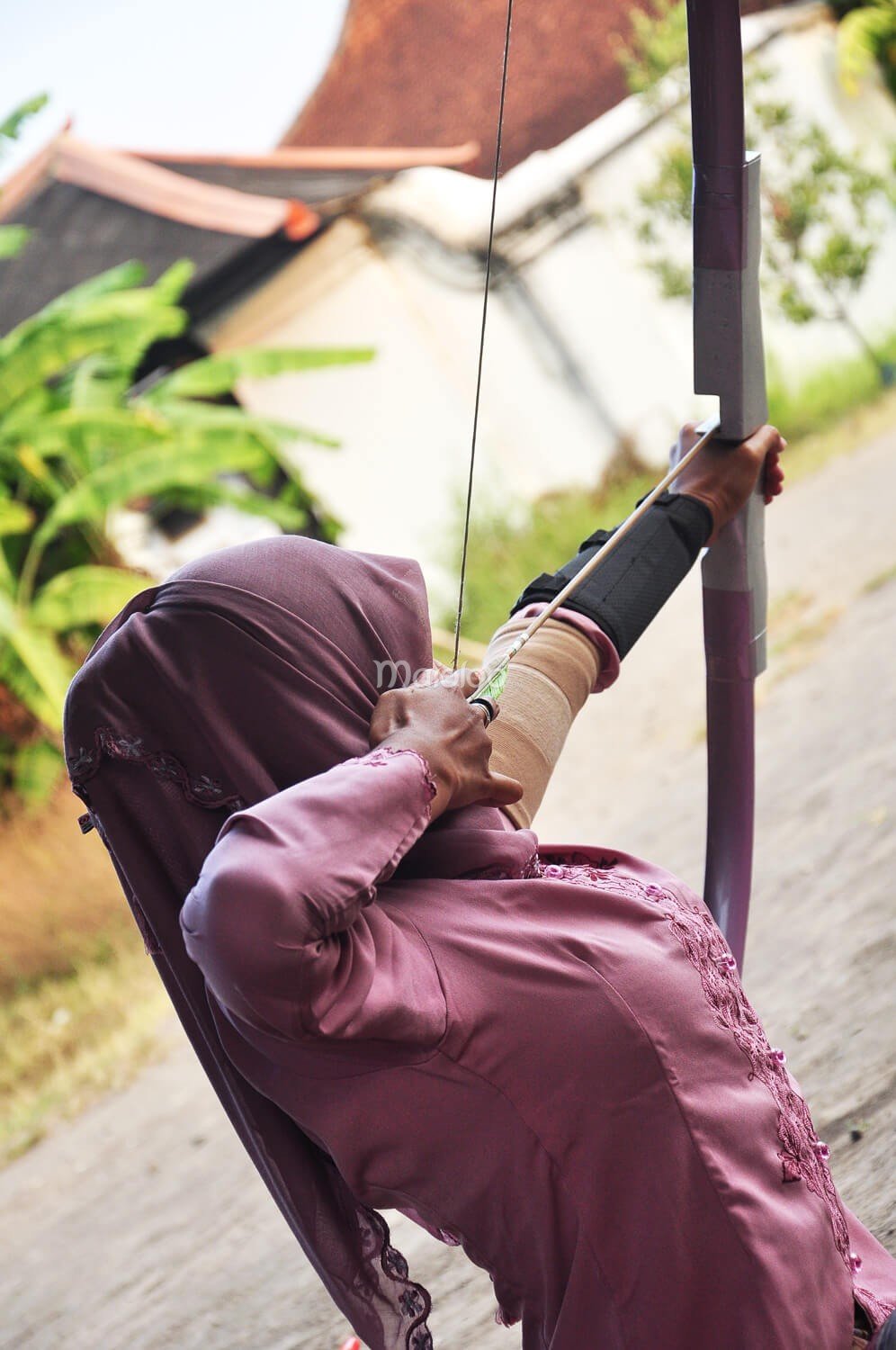 A participant in a pink outfit aims a bow and arrow at a target during Jemparingan.